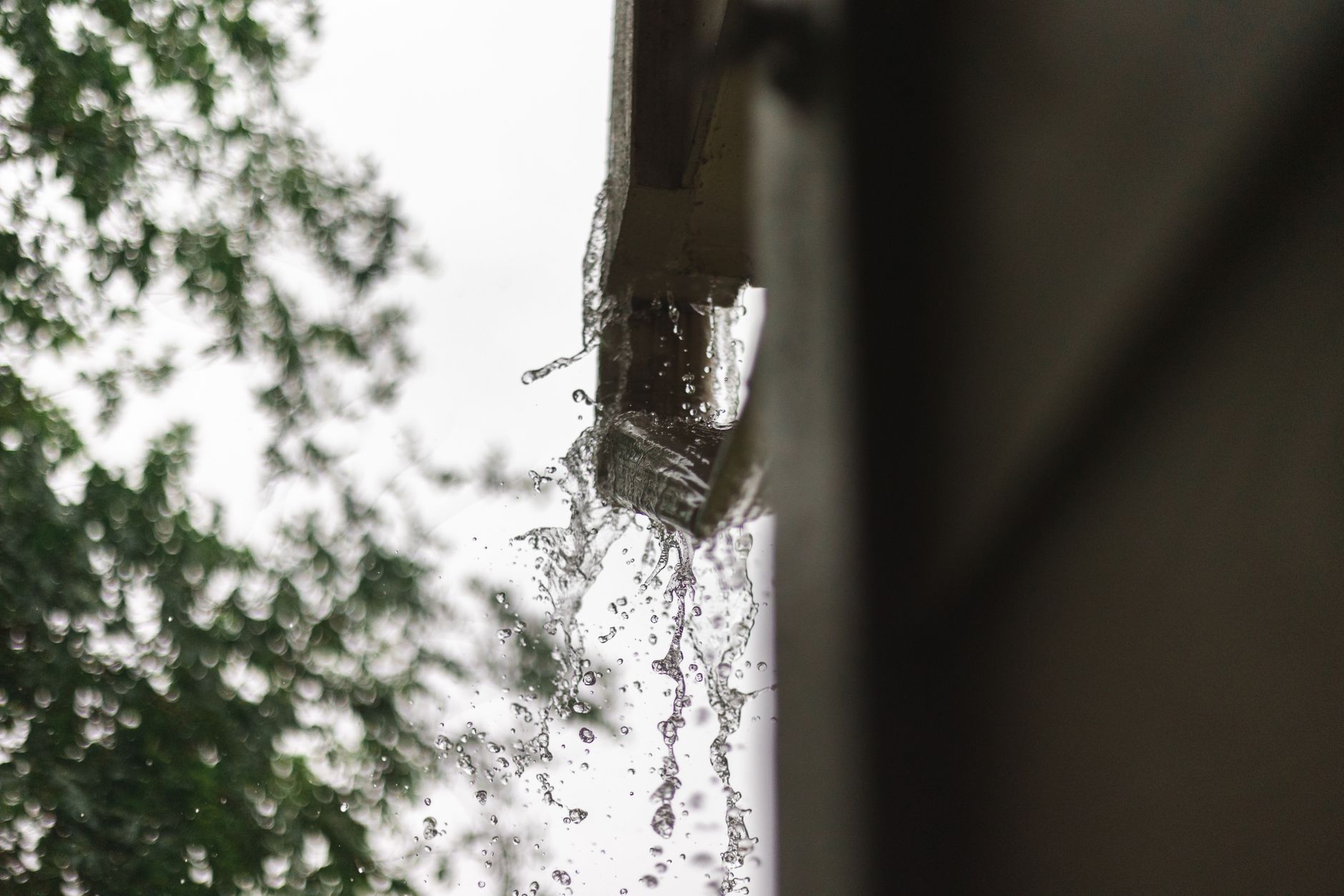 Regenwasser läuft an einer Dachrinne über und stürzt an der Hauswand herunter