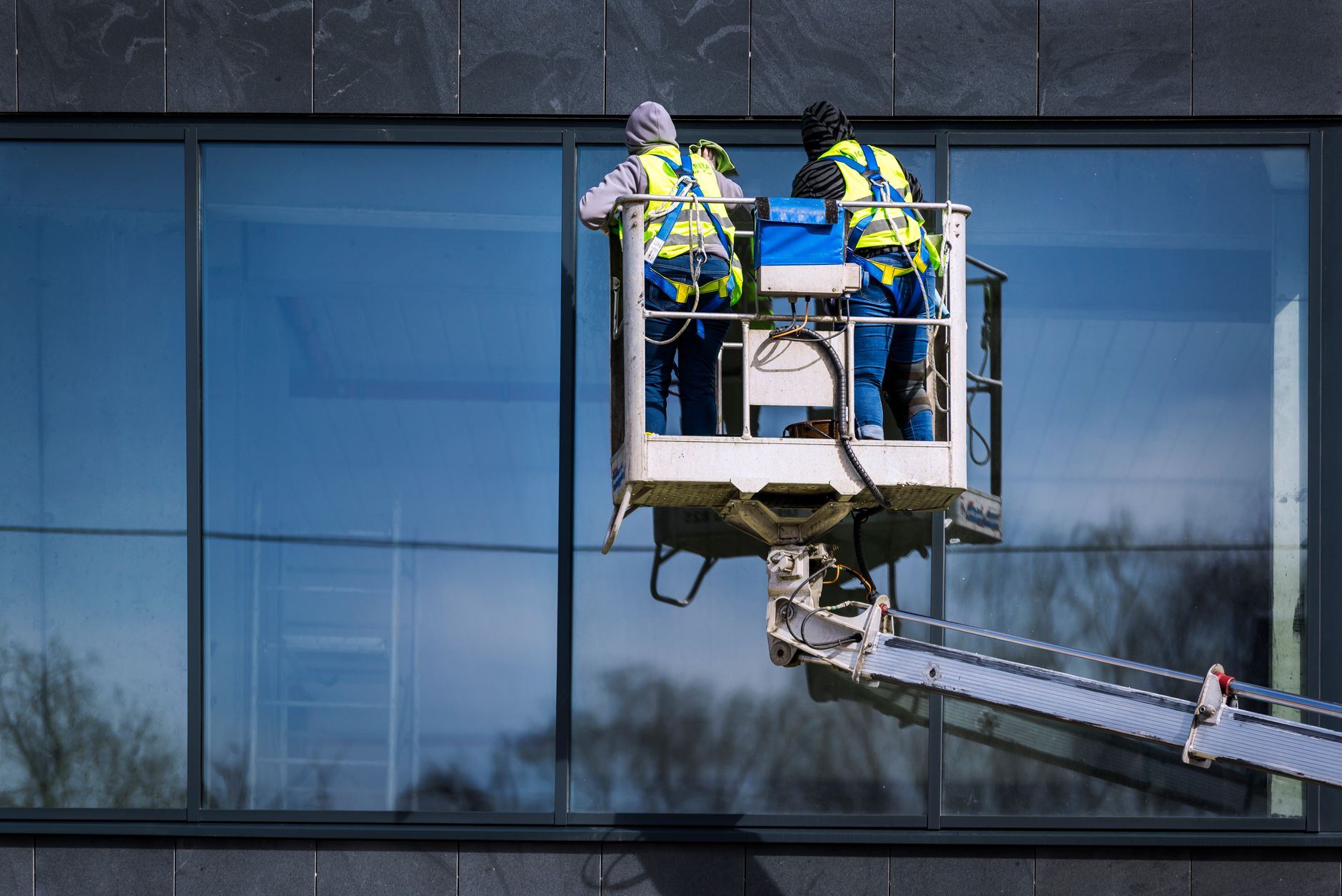 Zwei Fensterreiniger in einem Hubsteigerkorb reinigen die Glasfassade eines Bürogebäudes