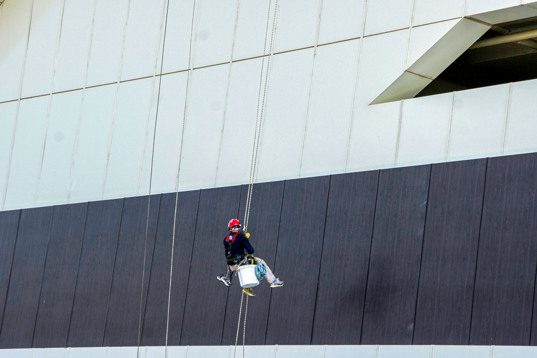 Industriekletterer mit Helm, Gurt und zwei Seilen bei der Arbeit an einer Gebäudefassade